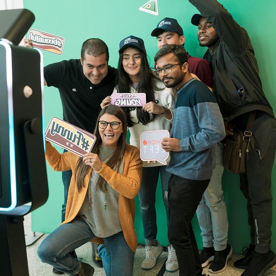 Group of students poses at the photo backdrop holding up hashtag signs.