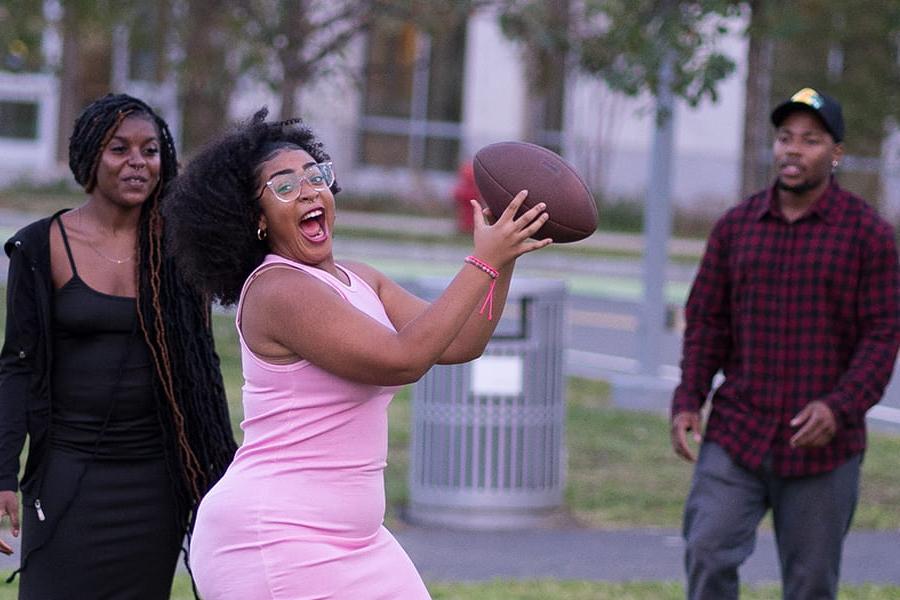 Student in pink dress catches a football.